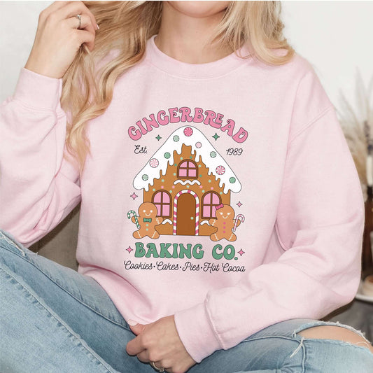 Sweatshirt rosa claro com ilustração retro de casinha e bonecos de gengibre, com o texto “Gingerbread Baking Co.”. Doçura e estilo natalício