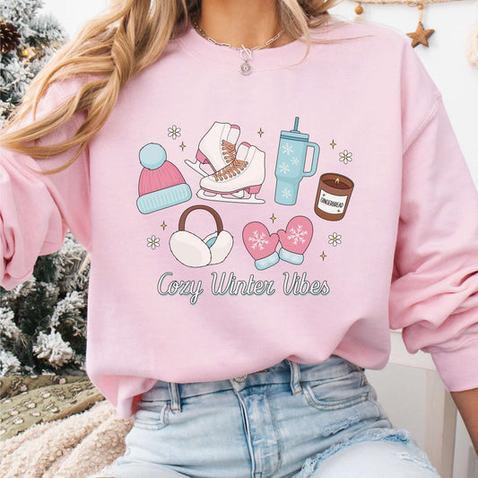 Sweatshirt Cozy Winter Vibes em rosa claro, com ilustrações fofas de inverno, como gorro, patins de gelo e vela de gengibre. Aconchego e estilo para os dias frios!