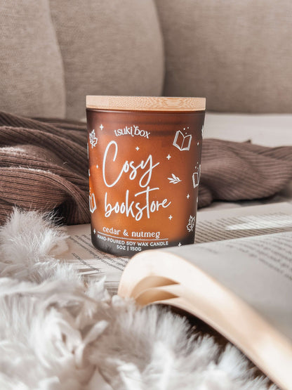 vela em pote ambar, em cima de livro aberto e mantinhas cosy